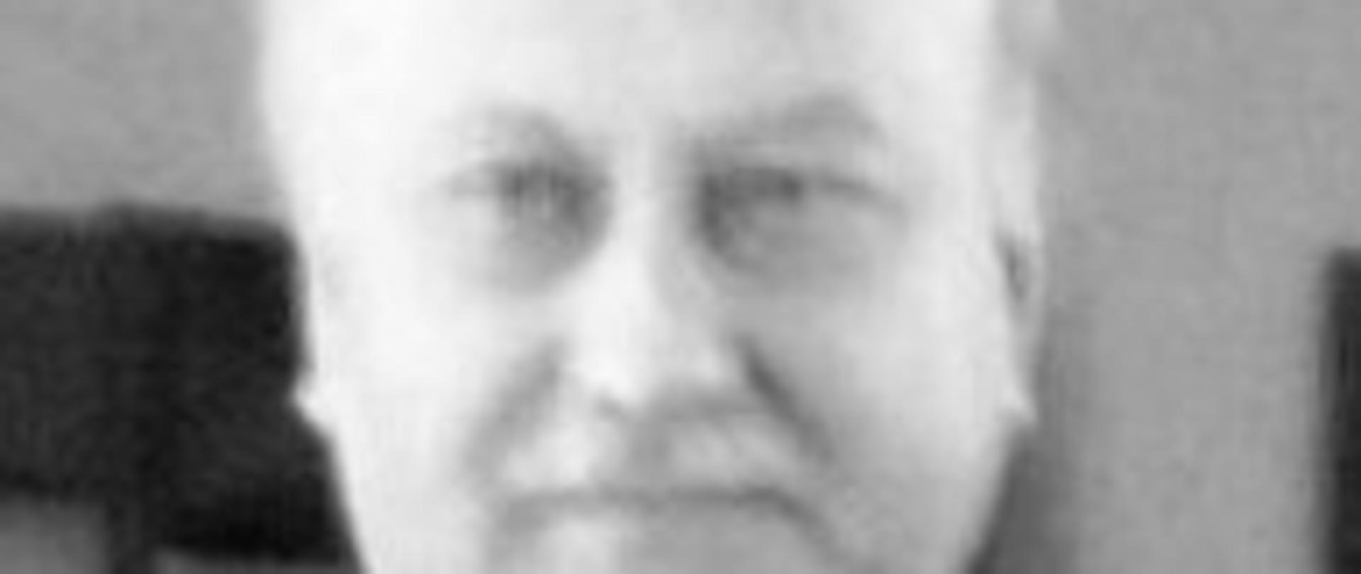 zdjęcie czarno białe przedstawia mężczyznę z wąsem w garniturze w białej koszuli i z krawatem