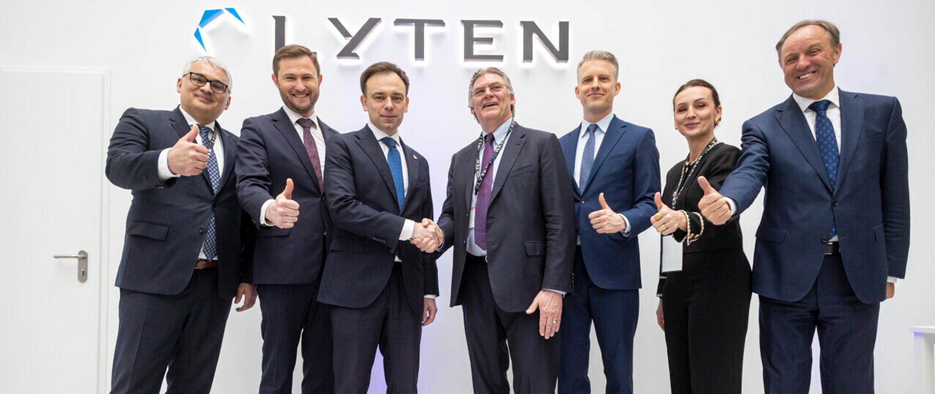 grupa osób stoi na scenie i podaje sobie ręce