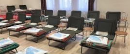 Zdjęcie przedstawia pomieszczenie remizy OSP z rozłożonymi łóżkami polowymi, przygotowane na ewentualny nocleg.Przy każdym łóżku znajduje się krzesło. 