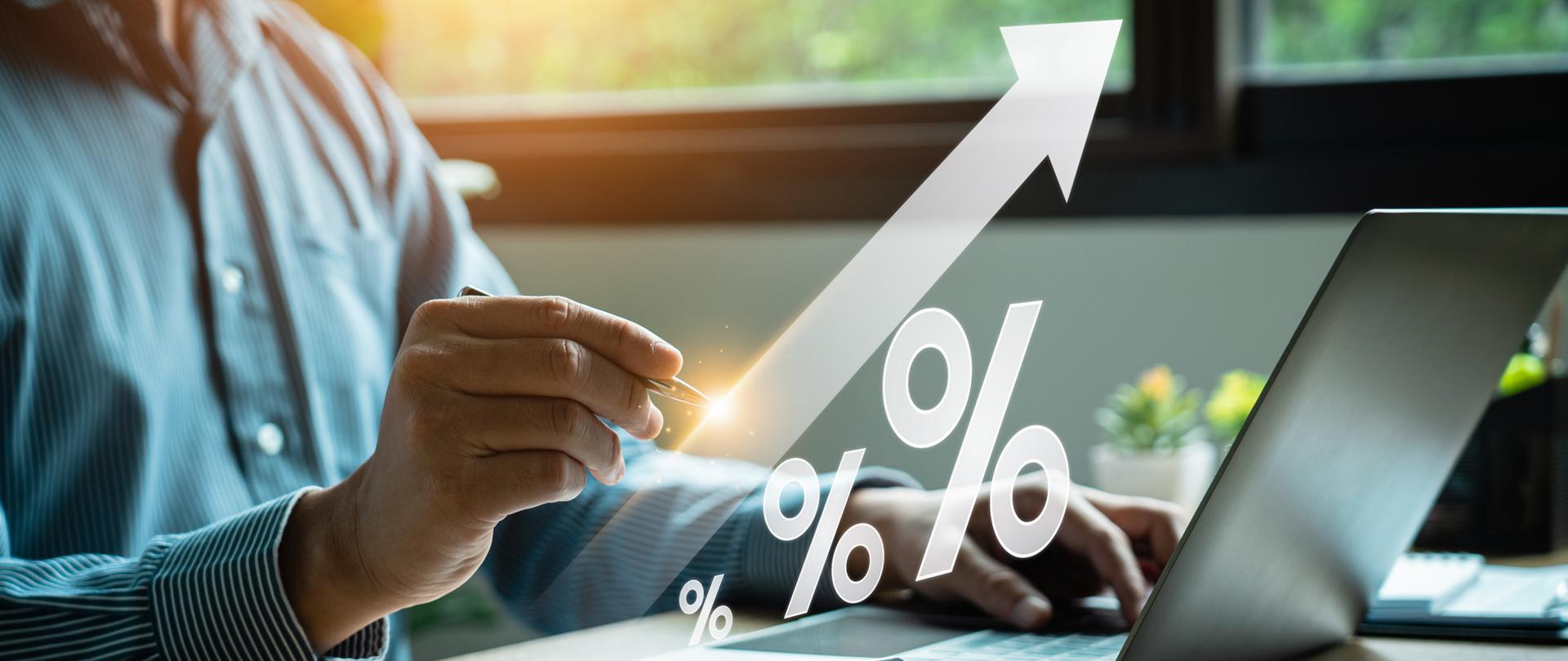 Dłonie mężczyzny przy biurku z kalkulatorem i otwartym laptopem. 