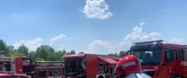 Zdjęcie przedstawia Kierującego Działaniem Ratowniczym (ćwiczeniami) na tle pojazdów pożarniczych