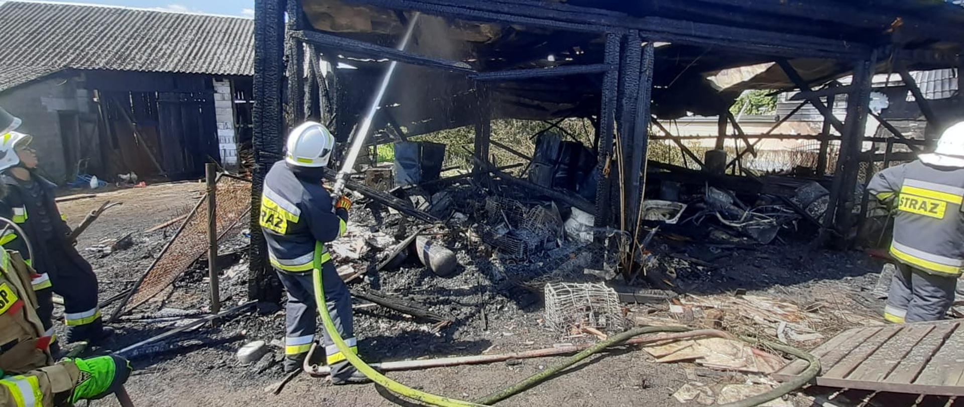 Pożar budynków gospodarczych w Brodach gm. Końskie. Strażacy OSP przelewają i dogaszają spaloną konstrukcję budynku gospodarczego.