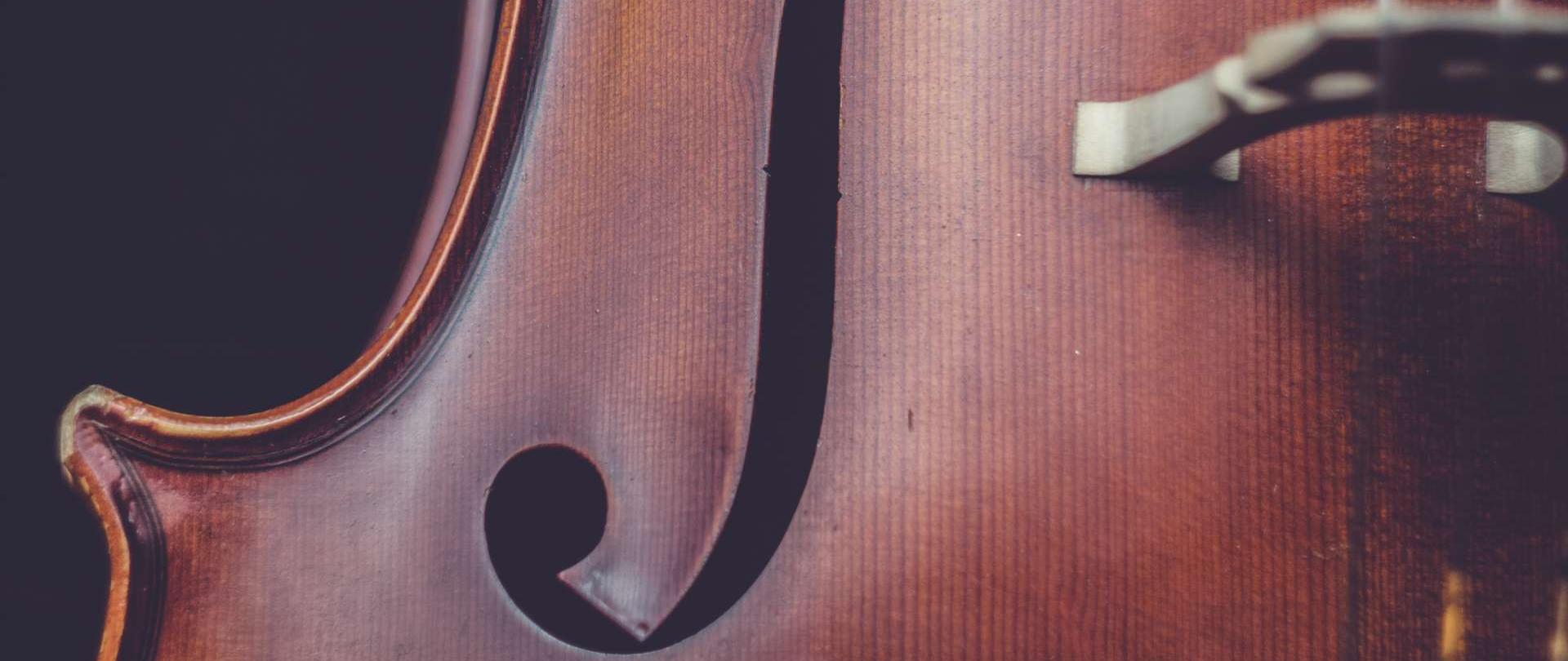 fotografia przedstawia fragment pudła rezonansowego wiolonczeli na czarnym tle