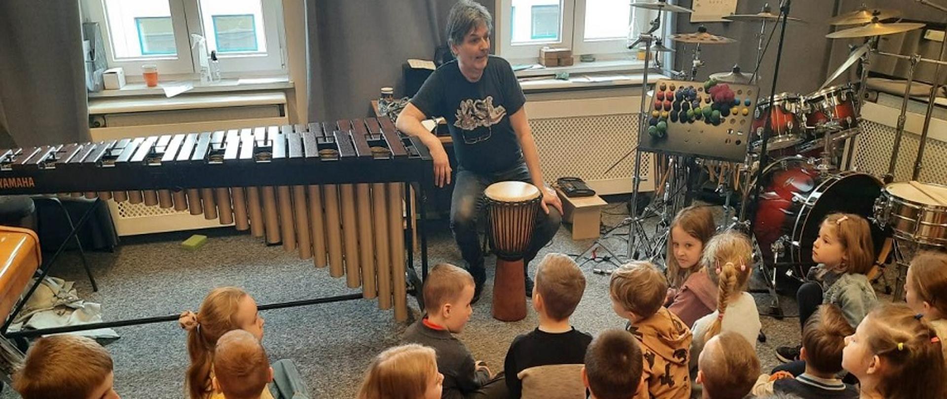 dzieci w wieku przedszkolnym w klasie wypełnionej instrumentami perkusyjnymi słuchające nauczyciela
