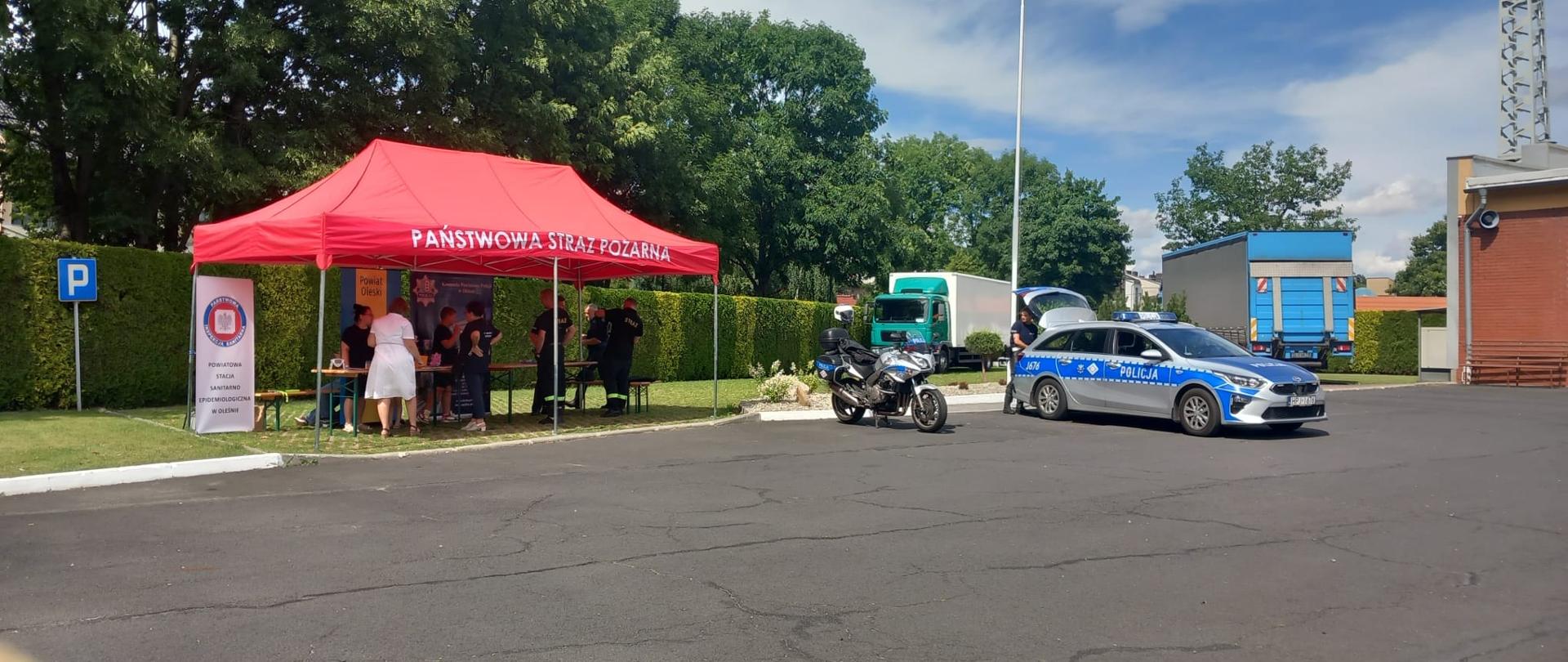 Namiot Państwowej Straży Pożarnej, obok motor i samochód policyjny.