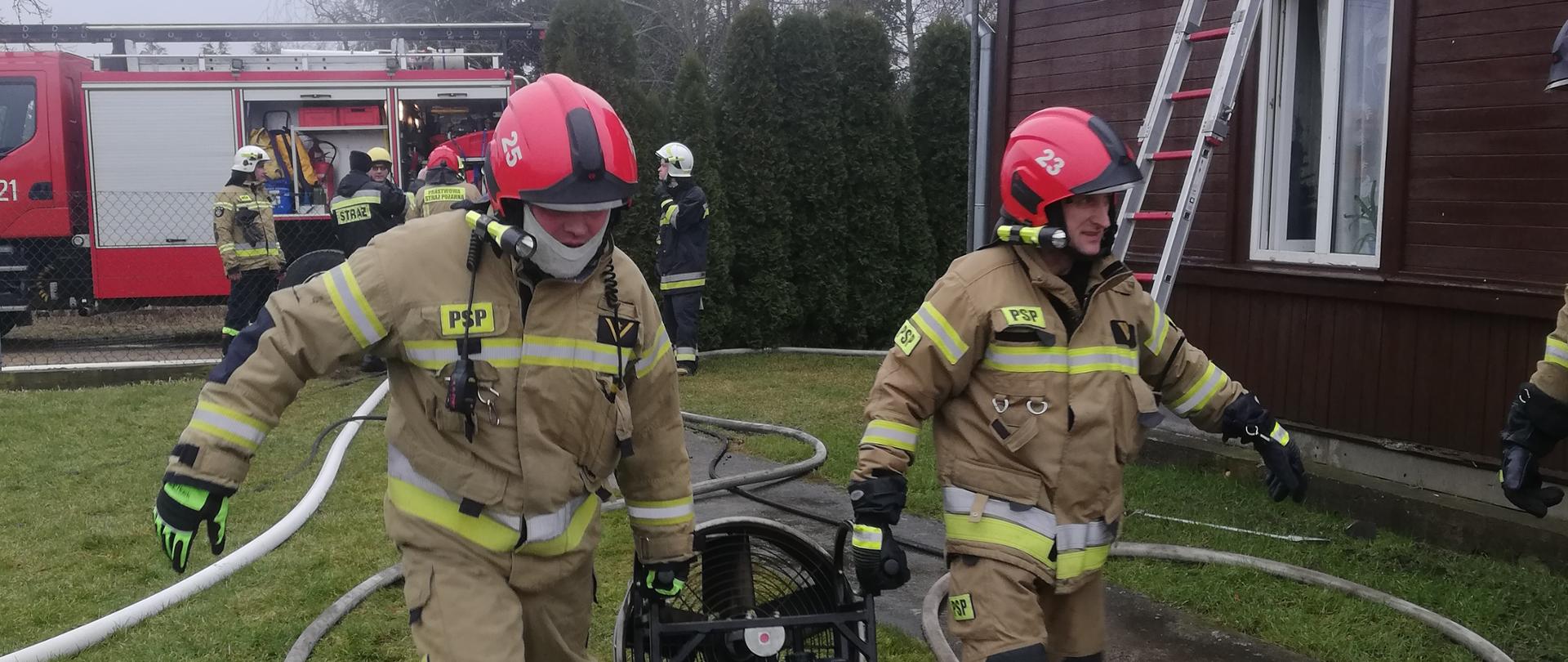 Strażacy PSP niosą wentylator oddymiający.