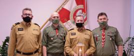 Zastępcy komendanta głównego PSP wraz z druhami pozują do zdjęcia stając naprzemiennie od lewej tj. zastępca komendanta oraz druh, jeden z zastępców trzyma lampion, w tle sztandar na ścianie
