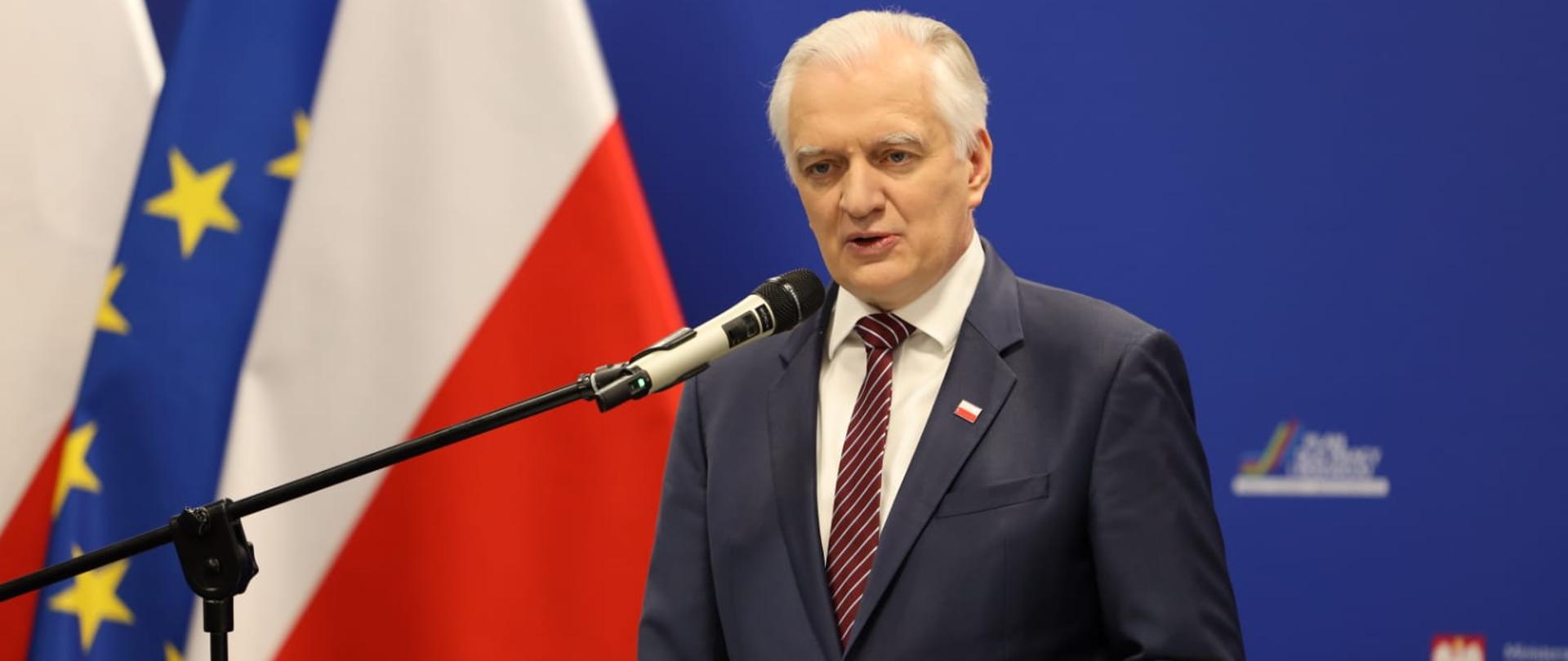 Wicepremier Jarosław Gowin przemawia zza mównicy. W tle flagi Polski i UE oraz ścianka z logotypami MRPiT.