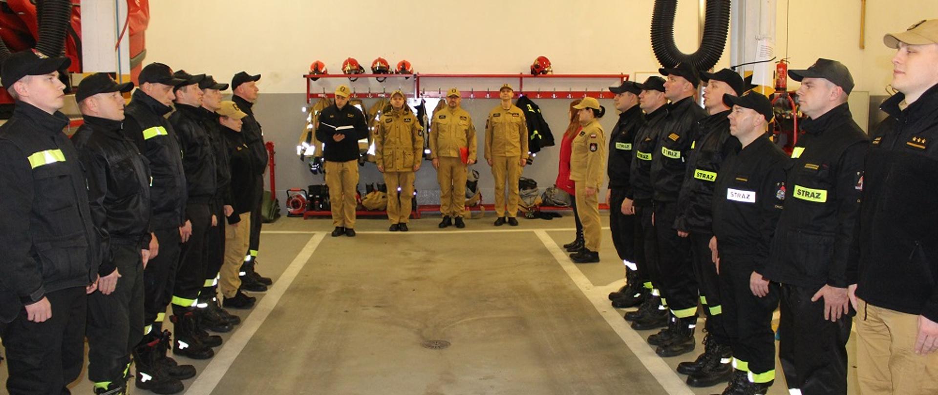 Zdjęcie przedstawia strażaków w trakcie uroczystego wręczania decyzji.
W tle pomieszczenie garaży JRG.
