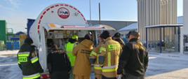 Zdjęcie przedstawia strażaków uczestniczących w warsztatach oraz pracownika firmy AirLiquide Polska Sp. z o.o. w trakcie praktycznego omówienia budowy zaworów w cysternie do przewozu cieczy kriogenicznych.