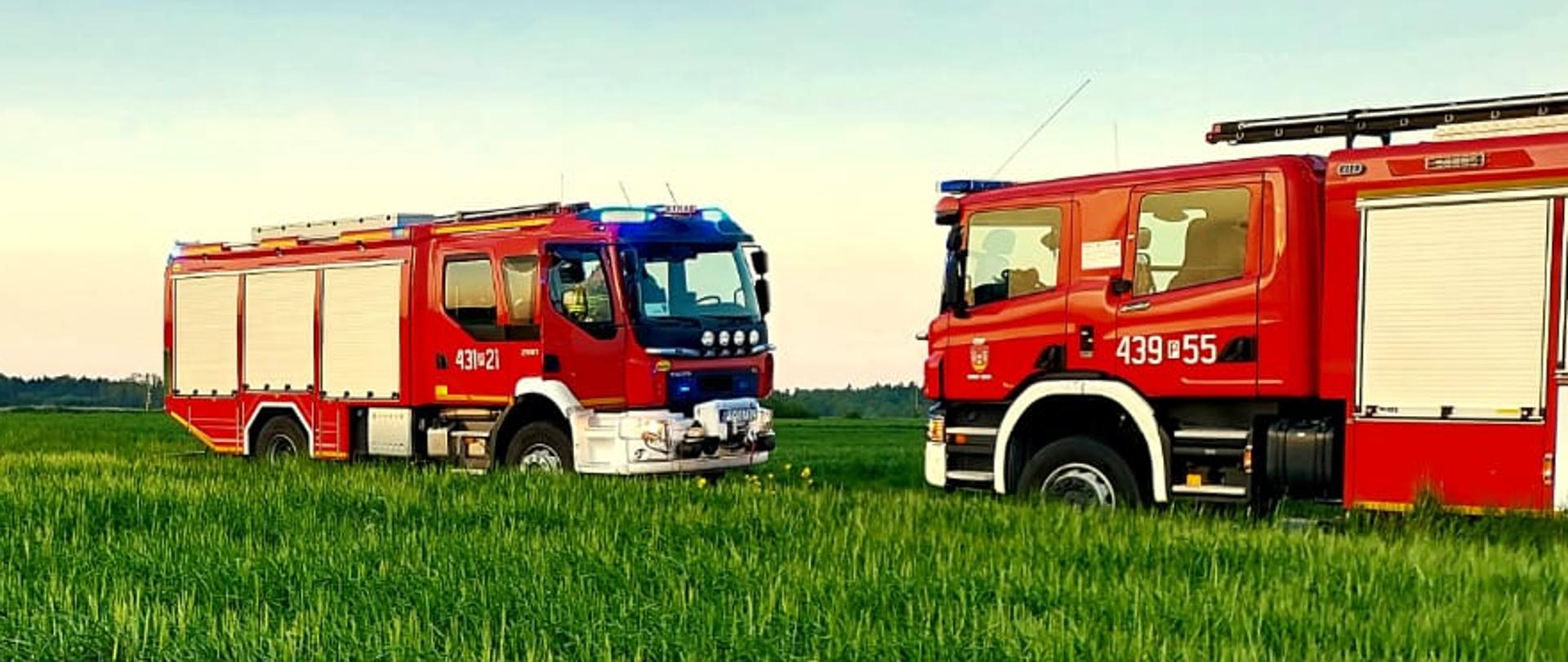 Zdjęcie przedstawia dwa wozy strażackie oraz samochód osobowy. Samochód znajduje się poza jezdnią w polu.