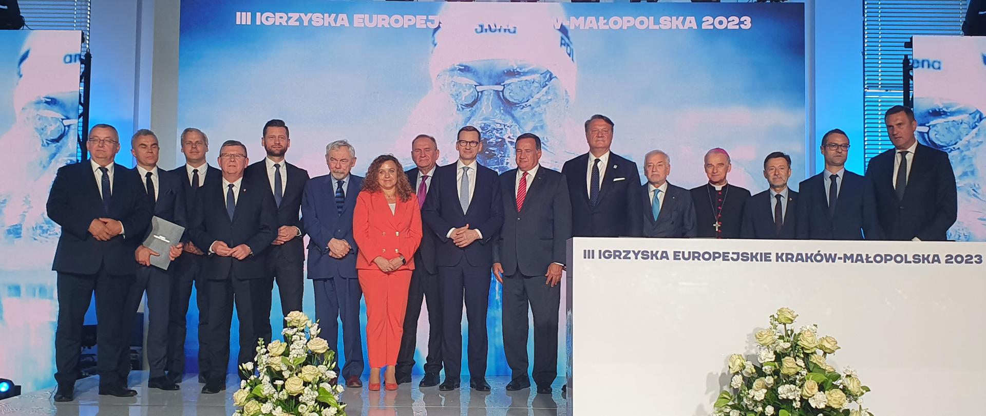 Uroczyste podpisanie umowy host city przed III Igrzyskami Europejskimi Kraków-Małopolska 2023. Na scenie w Centrum Olimpijskim stoją zaproszeni goście - premier Mateusz Morawiecki, Minister Kamil Bortniczuk, przedstawiciele krakowskiego samorządu, sygnatariusze umowy.