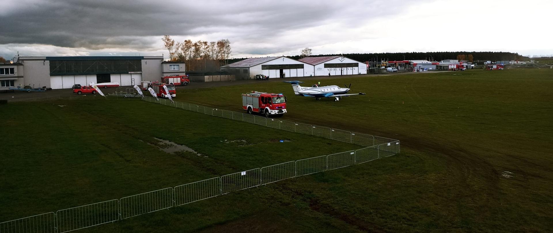 Samochody strażackie stoją na płycie lotniska obok samolotu.