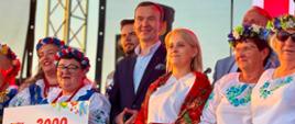 wicewojewoda stoi na scenie z kobietami w ludowych strojach trzymające czek pieniężny oraz inne nagrody 