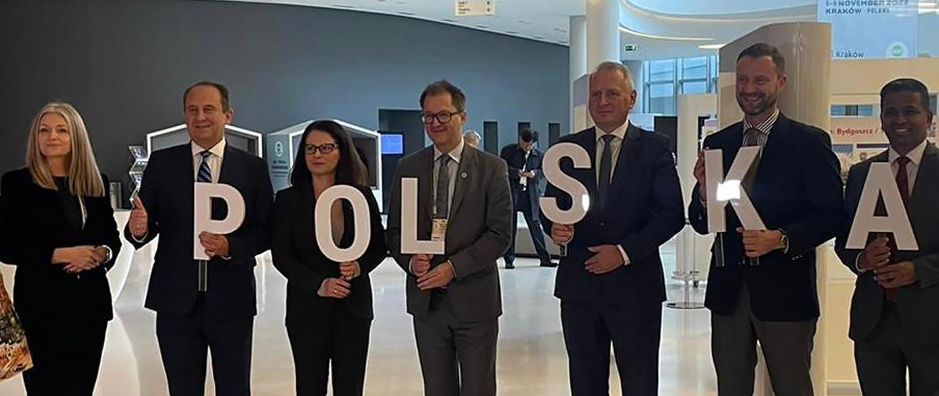Sekretarz stanu Andrzej Gut-Mostowy w trakcie ICCA w Krakowie - organizatorzy i goście kongresu stoją w holu centrum kongresowego, trzymając w rękach litery układające się w napis POLSKA