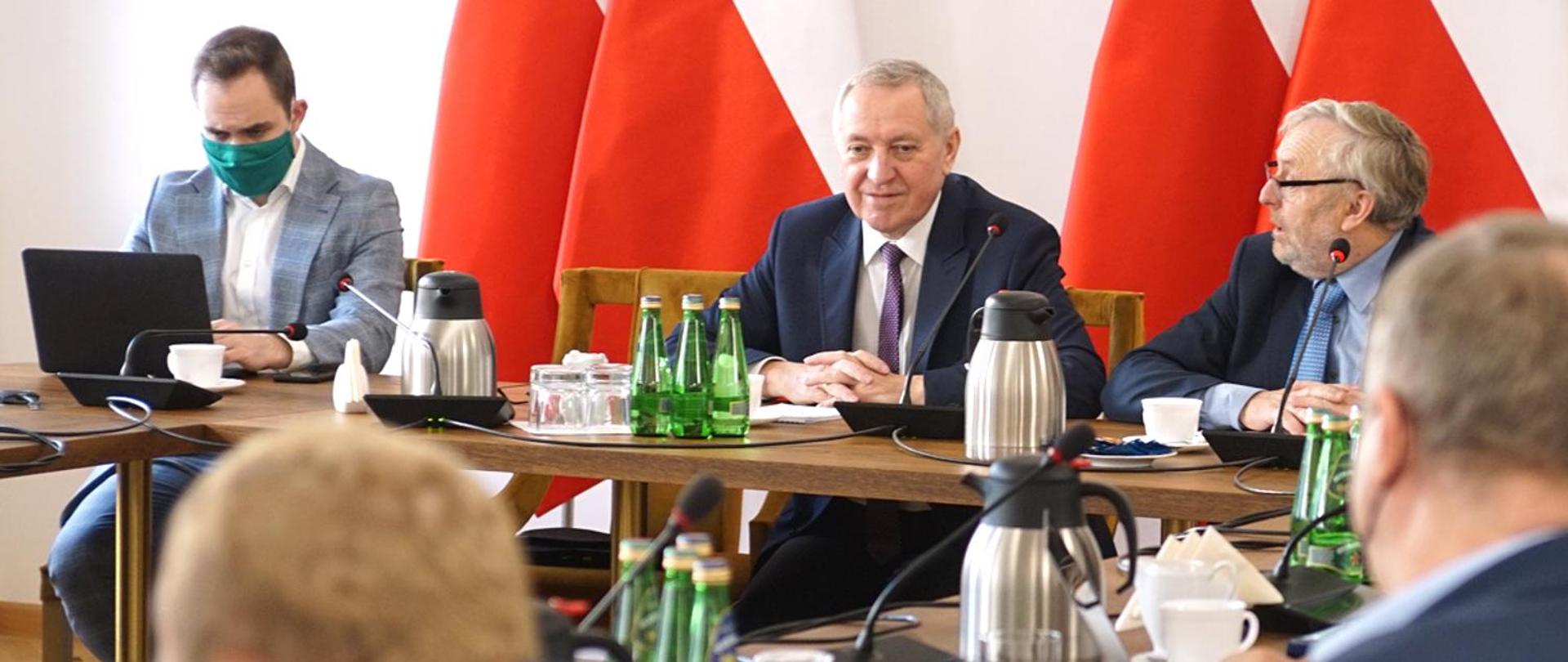 Wicepremier, ministra rolnictwa i rozwoju wsi Henryk Kowalczyk podczas spotkania, siedzący przy stole na tle biało-czerwonych flag