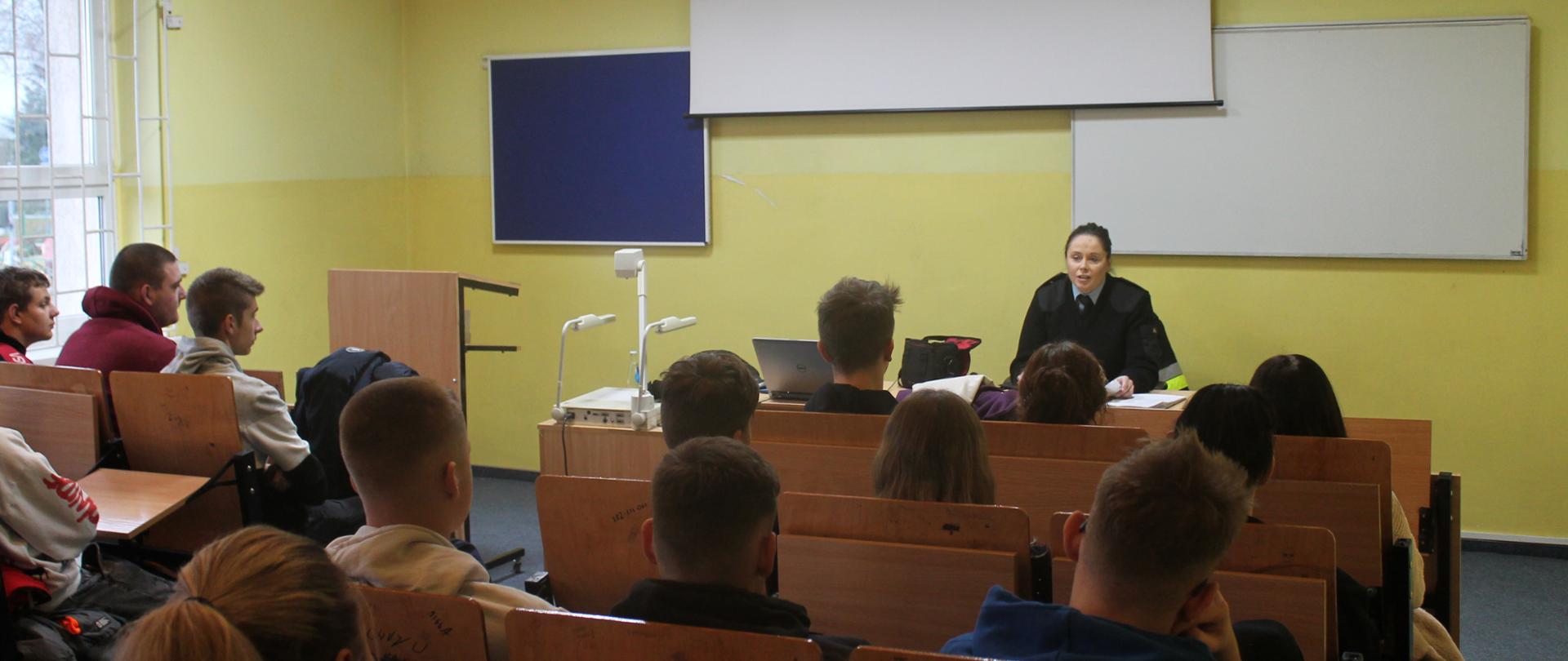 Zdjęcie przedstawia strażaka i uczniów podczas spotkania dotyczącego propagowania zawodu oficera w PSP