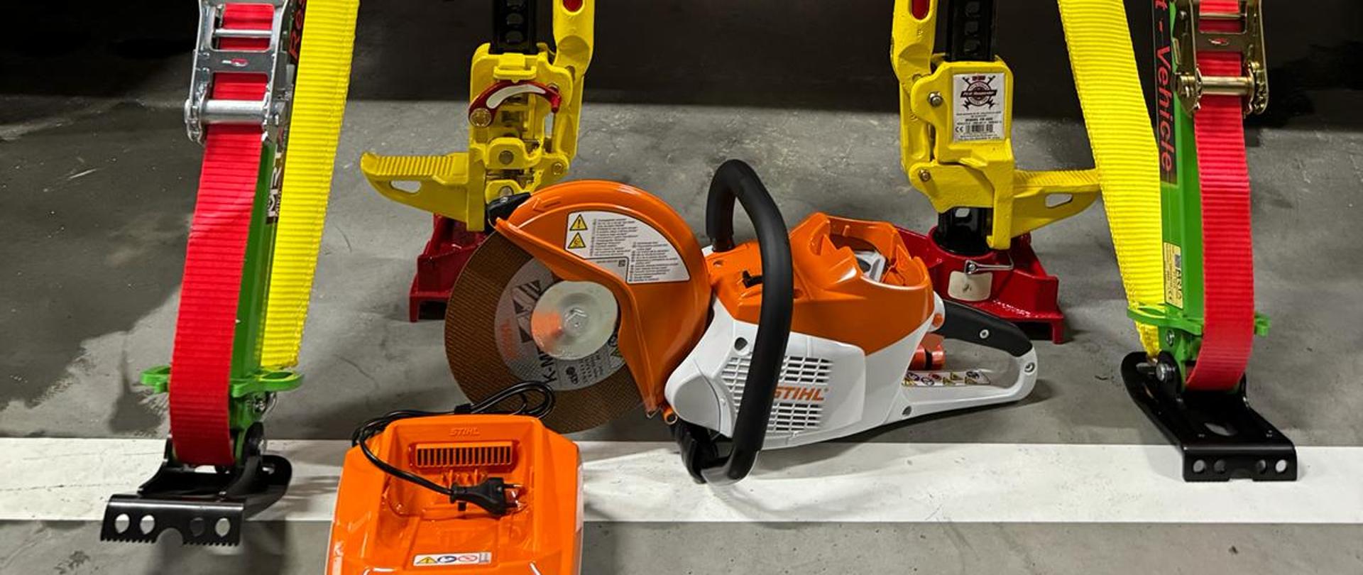 W garażu na tle pojazdu pożarniczego stoi sprzęt pożarniczy. Obok stoi tabliczka z napisem Orlen dla strażaków.