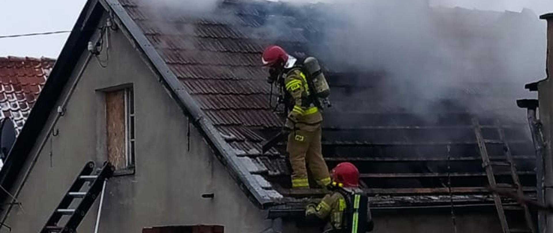 pora dzienna, dwóch strażaków PSP w aparatach OUO gasi dymiący się dach, częściowo rozebrany.