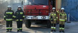 Widok z przodu. Czterech strażaków OSP Targanice Dolne stoi w ubraniach specjalnych przed samochodem pożarniczym przed garażem OSP. 
