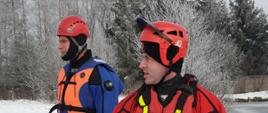Dwóch strażaków zabezpieczonych w skafandry do ratownictwa lodowego stoi na brzegu zbiornika.