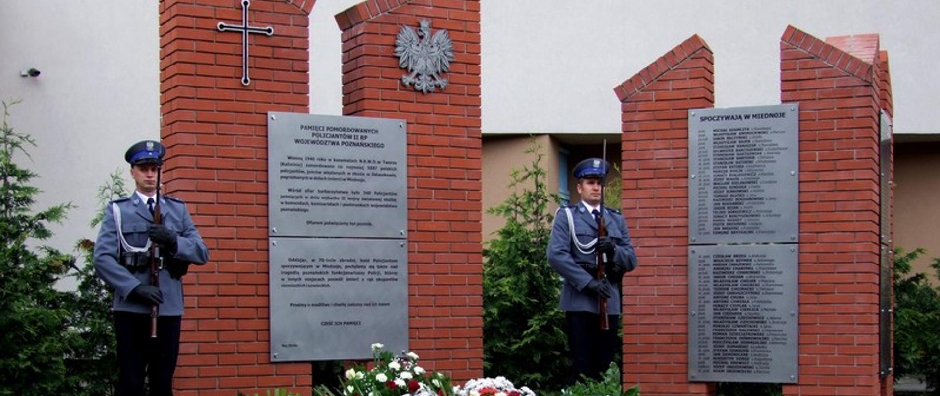 pomnik przy którym dtoi dwóch policjantów i leżą biało czerwone wiązanki 