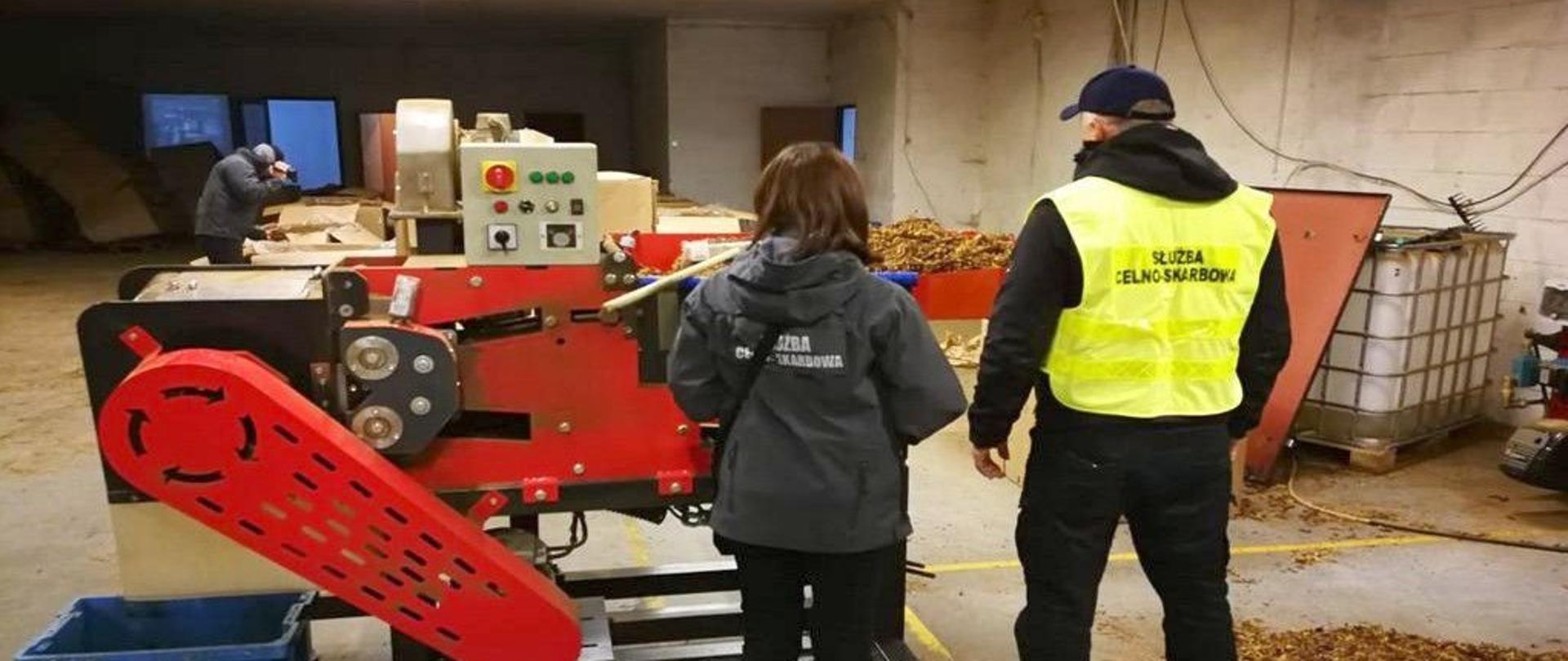 Pracowniczka i funkcjonariusz KAS przy maszynie do przetwarzania tytoniu.