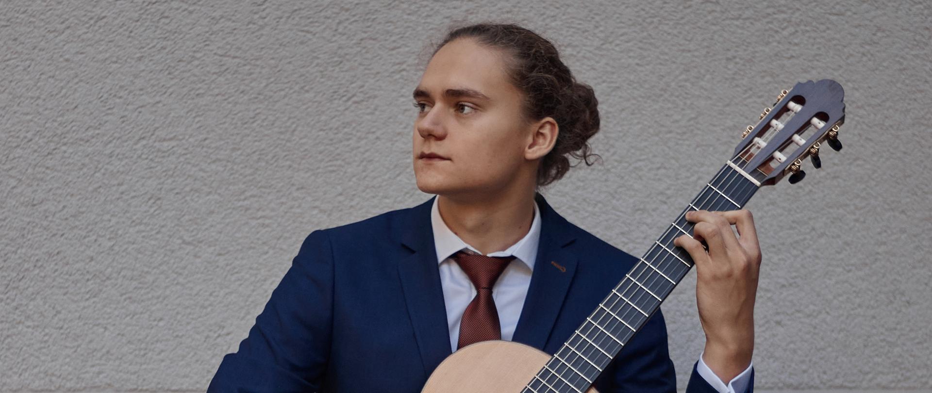 Na zdjęciu Matusz Wójcik z gitarą siedzący na ławce.