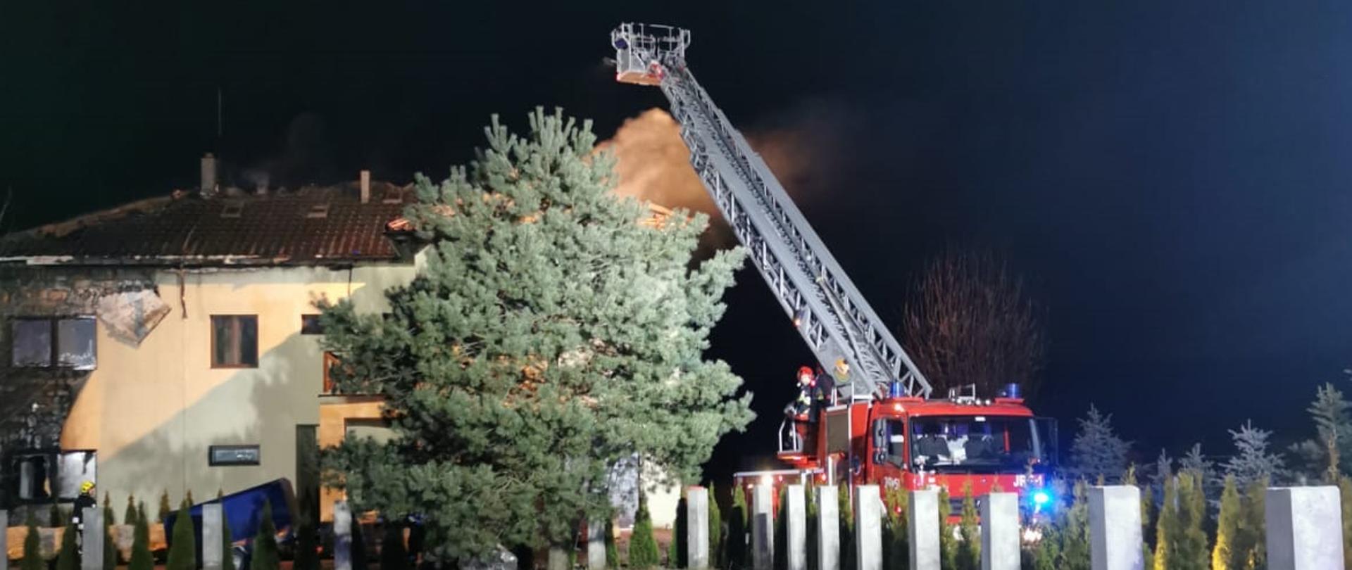 Na zdjęciu w oddali widać budynek mieszkalny, na którym paliła się elewacja oraz dach. W prawej części zdjęcia znajduje się podnośnik SCD-37, z którego prowadzone są działania gaśnicze oraz rozbiórka spalonej części dachu.