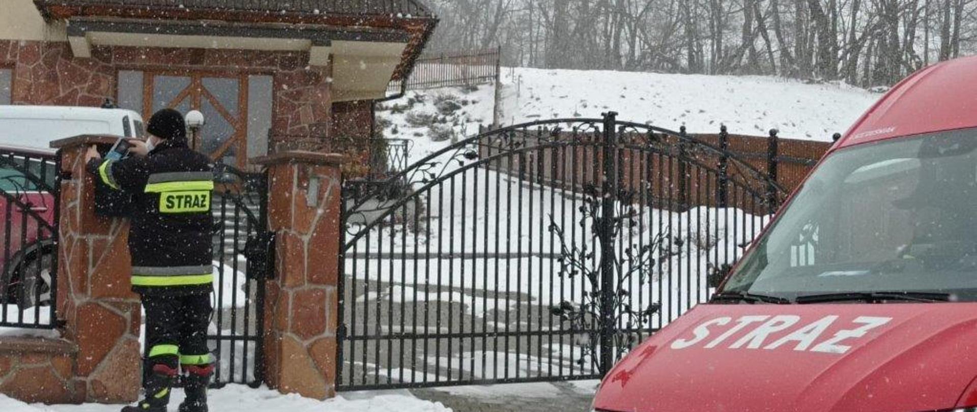 Strażak wrzuca to skrzynki domu mieszkalnego ulotki. Po prawej stronie pojazd strażacki.