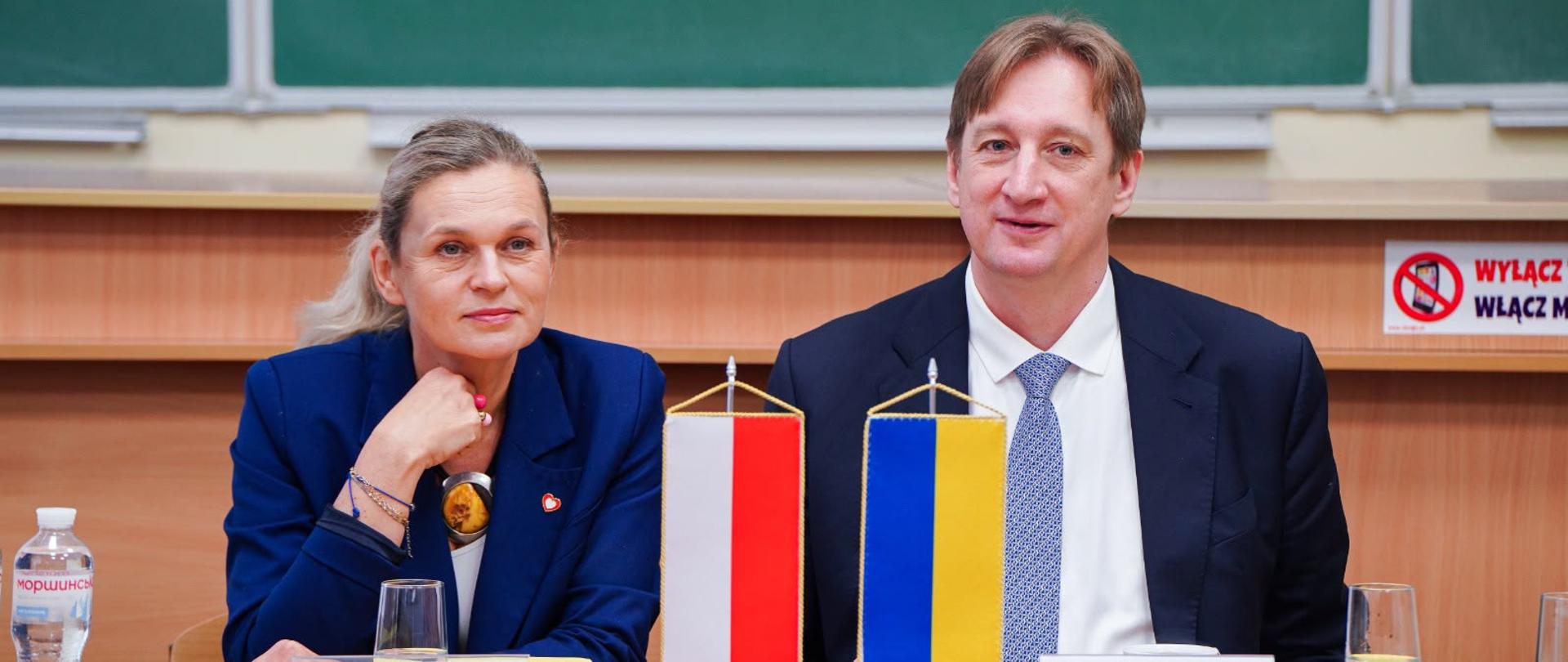 Minister Edukacji siedzi przy stole. Obok niej siedzi Minister Edukacji Ukrainy. Na stole stoją flagi Polski i Ukrainy oraz winietki. 