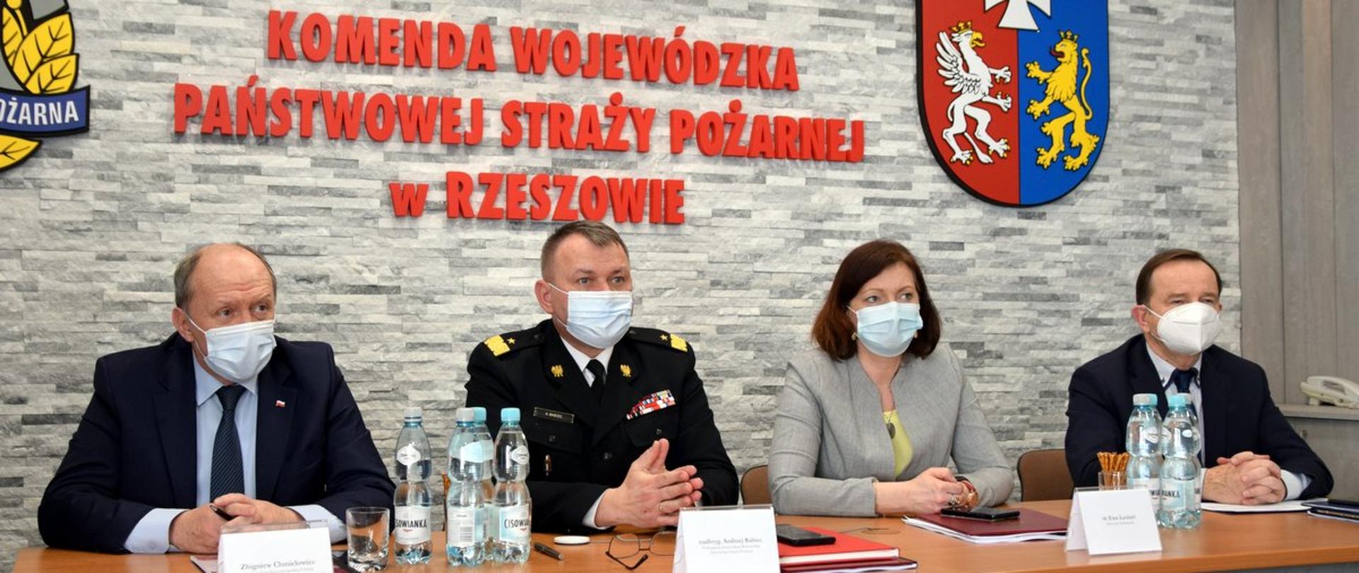 na zdjęciu stół prezydialny sali konferencyjnej. Za stołem od lewej strony: poseł na sejm RP Zbigniew Chmielowiec, podkarpacki komendant wojewódzki PSP nadbryg. Andrzej Babiec, wojewoda podkarpacki Ewa Leniart, marszałek województwa podkarpackiego Władysław Ortyl. W tle widać fragment logo PSP, pośrodku napis Państwowej Straży Pożarnej w Rzeszowie, a po prawej stronie fragment herbu województwa podkarpackiego. 