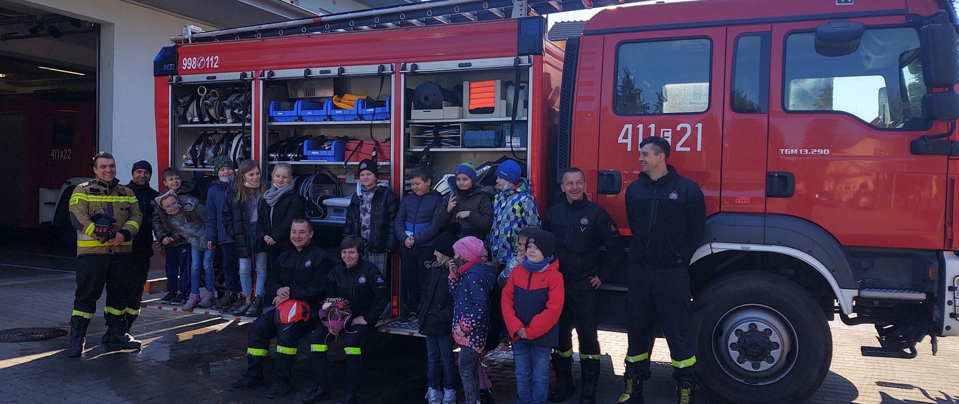 Na zdjęciu widać młodzież szkolną i strażaków ustawionych w szeregu do przed samochodem gaśniczym