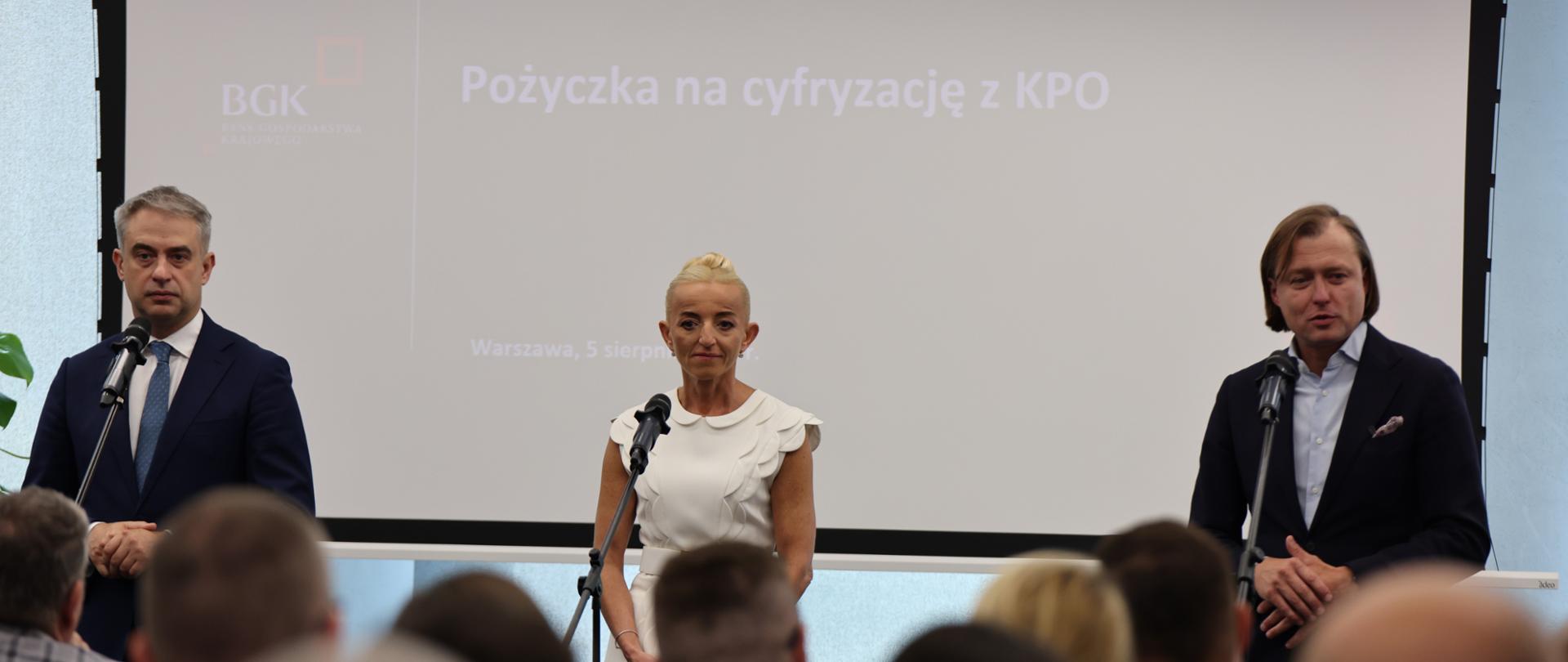 Na zdjęciu dwóch mężczyzn i kobieta po środku. Wszyscy przy mikrofonach.