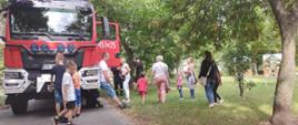Samochód gaśniczy zaparkowany w parku. Wokół auta osoby oglądające sprzęt i wyposażenie. 