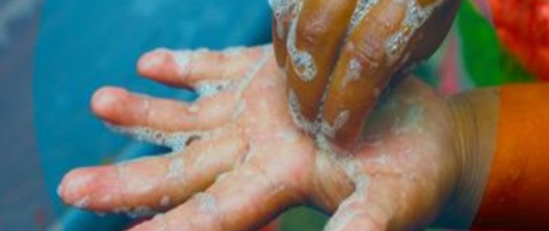 Dłoń osoby dorosłej myjącą rękę dziecka.