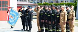 Na pierwszym planie pododdział strażaków ustawionych w szyku na placu komendy