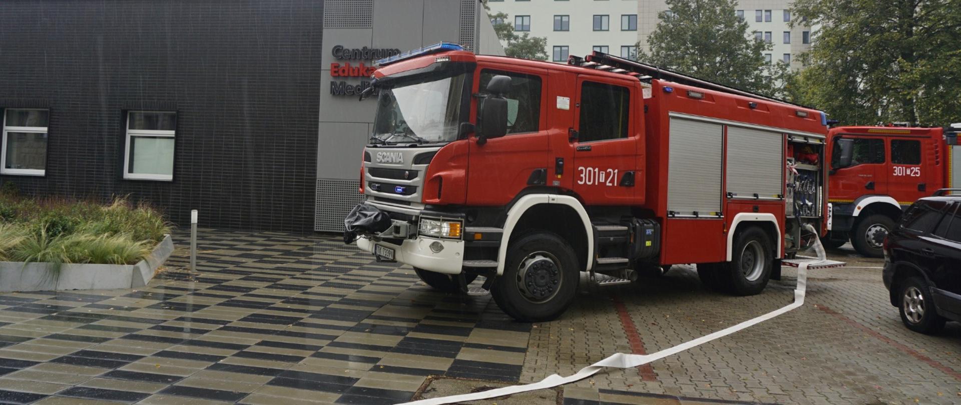 Zdjęcie przedstawia dwa samochody gaśnicze stojące przy budynku Centrum Edukacji Medialnej.