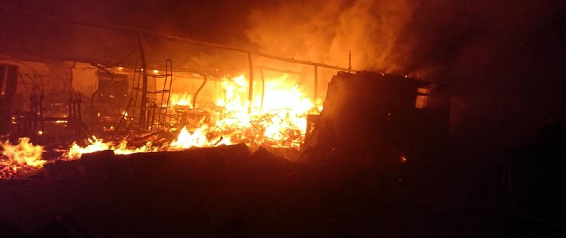 Na zdjęciu wykonanym w ciemnościach widać płonące wnętrze budynku magazynowego. Wszystko co pozostało wewnątrz uległo całkowitemu spaleniu.