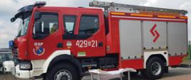 Nowy samochód gaśniczy OSP stoi na placu. Przed nim stolik z białym nakryciem.
