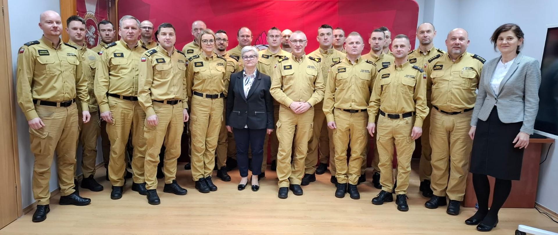 Strażacy pozują do zdjęcia na tle ścianki w świetlicy