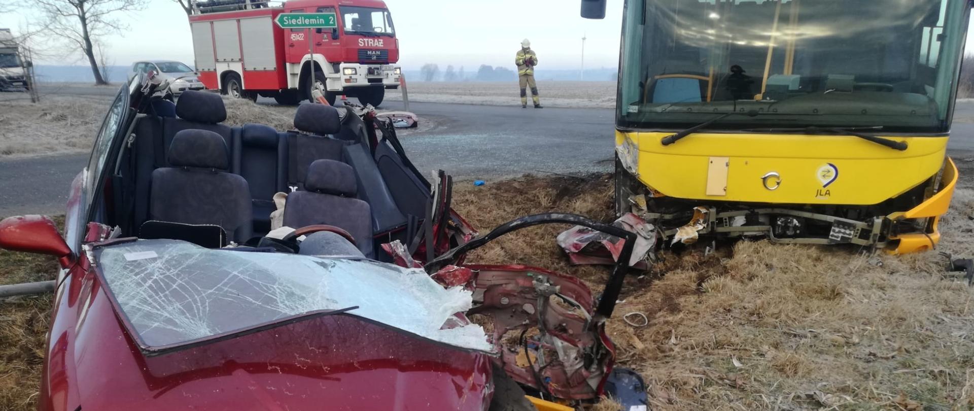 Wrak samochodu po wypadku, w tle uszkodzony autobus