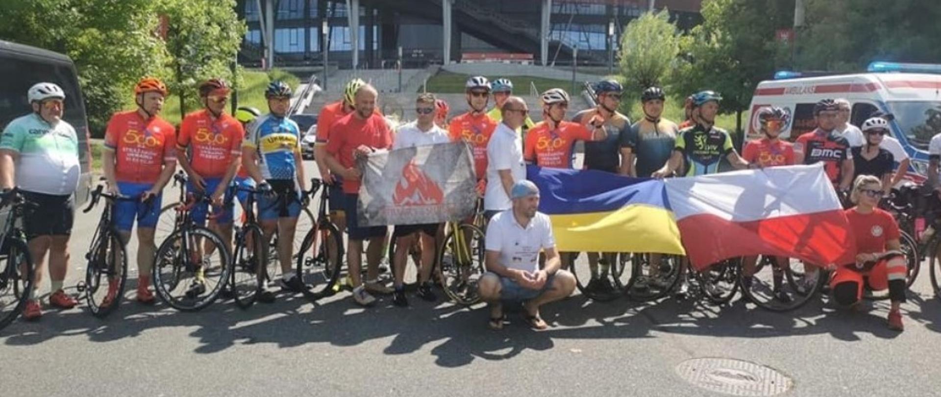 Kolarze stoją pod Stadionem Narodowym trzymając flagi Polski oraz Ukrainy.