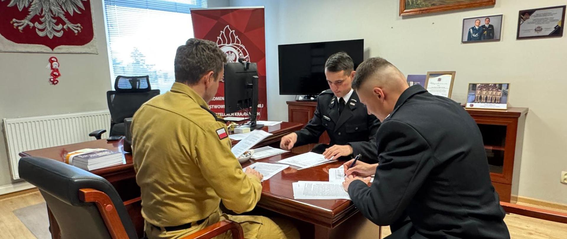 Fotografia przedstawia druhów OSP oraz Komendanta Powiatowego PSP podpisujących w gabinecie Komendanta umowy dotyczące uzyskania uprawnień kategorii C