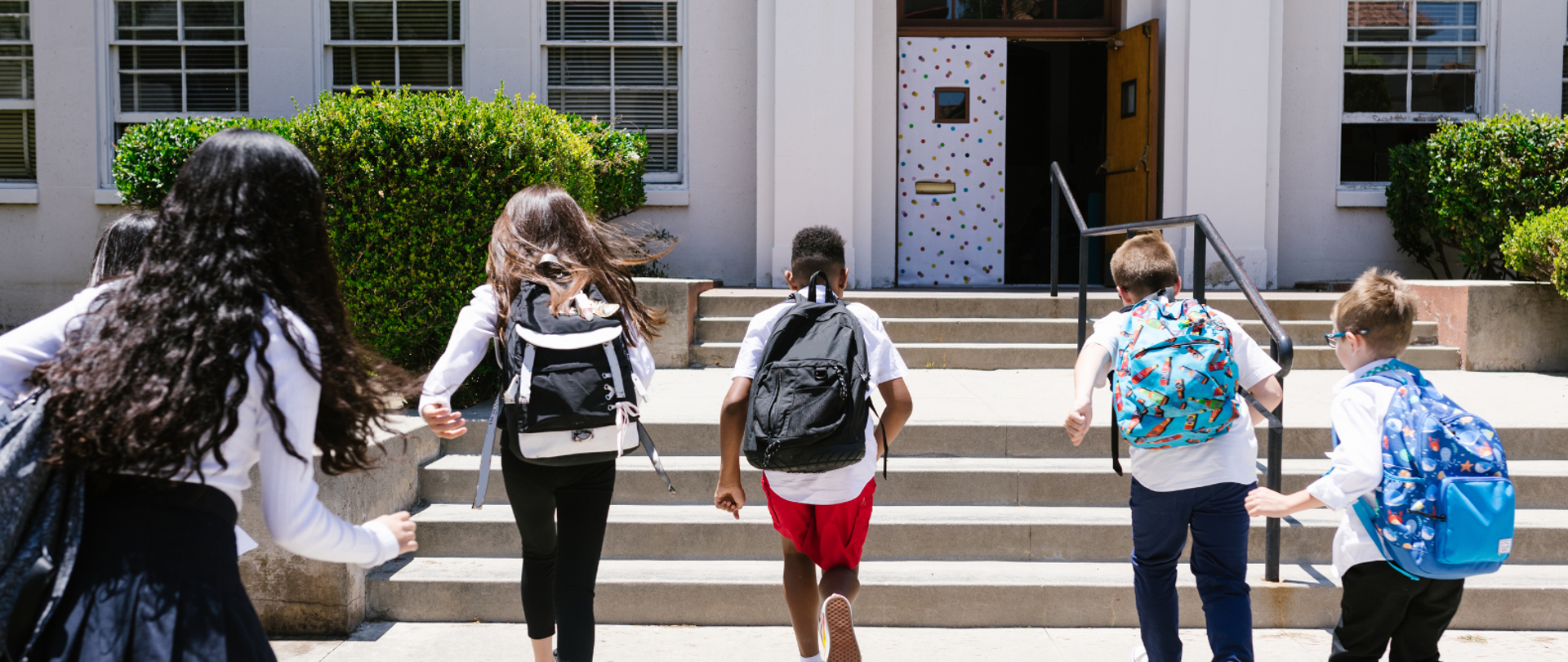 Zdjęcie przedstawiające dzieci wbiegające do szkoły z plecakami