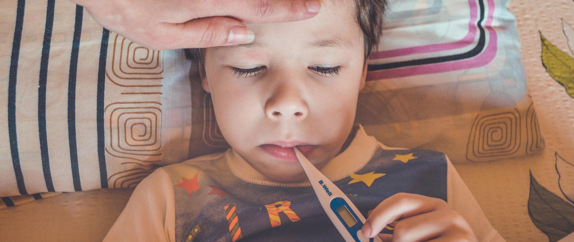 Zdjęcie przedstawiające chore dziecko, któremu mama mierzy temperaturę