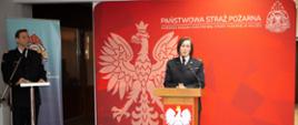 Strażak przemawia przy mównicy na tle banera PSP.
