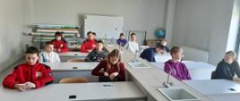 Uczestnicy Ogólnopolskiego Turnieju Wiedzy Pożarniczej przygotowuja się do testu pisemnego, siedzą w białych ławka na sali szkolnej