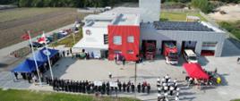 Zdjęcie przedstawia strażaków, druhów oraz zaproszonych gości stojących przed budynkiem remizy. 