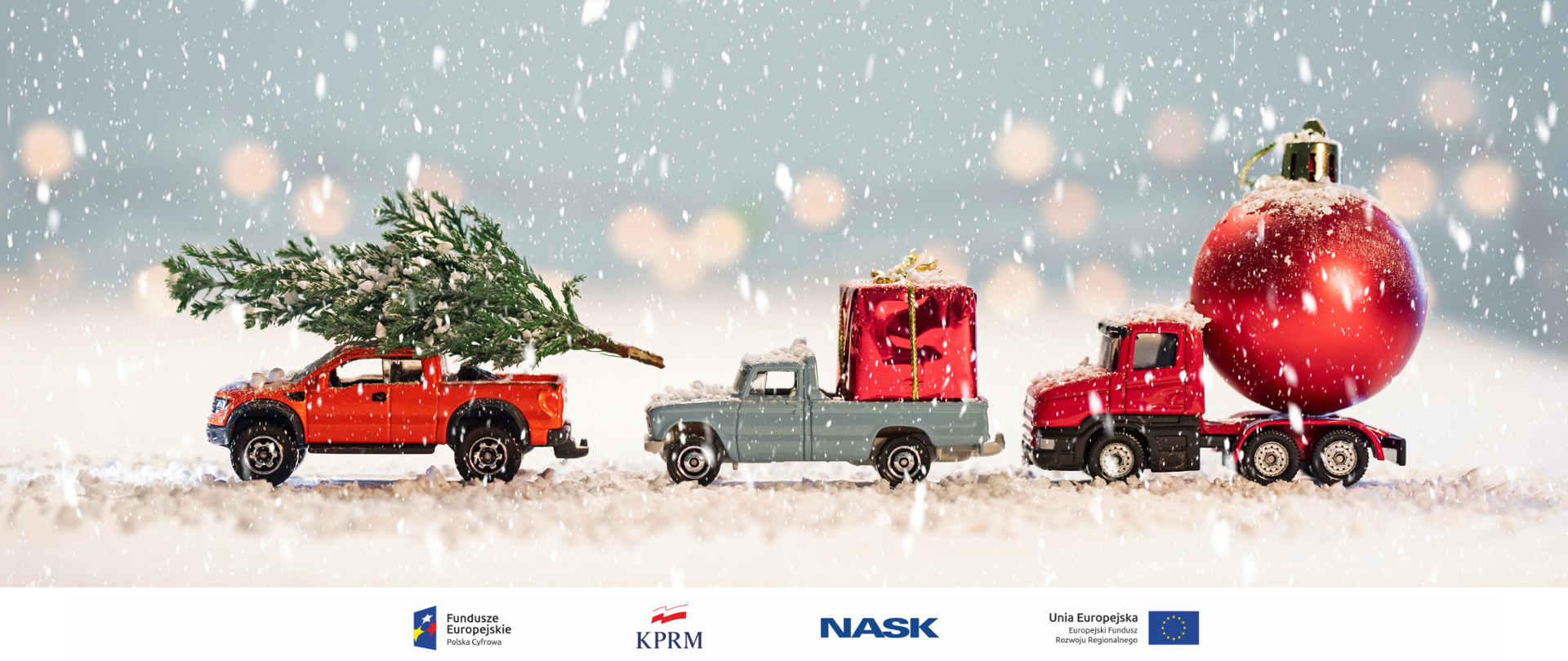 Zdjęcie stojących bokiem trzech małych zabawkowych samochodów w śniegu - na pierwszym choinka, na drugim - prezent , na trzecim - świąteczna bombka. 